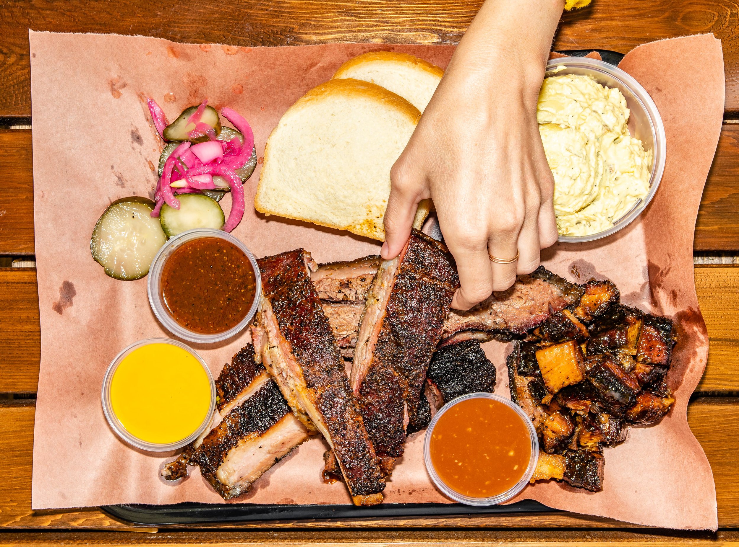 A close-up barbecue tray with smoked meat, sauce, pickles, and sliced bread