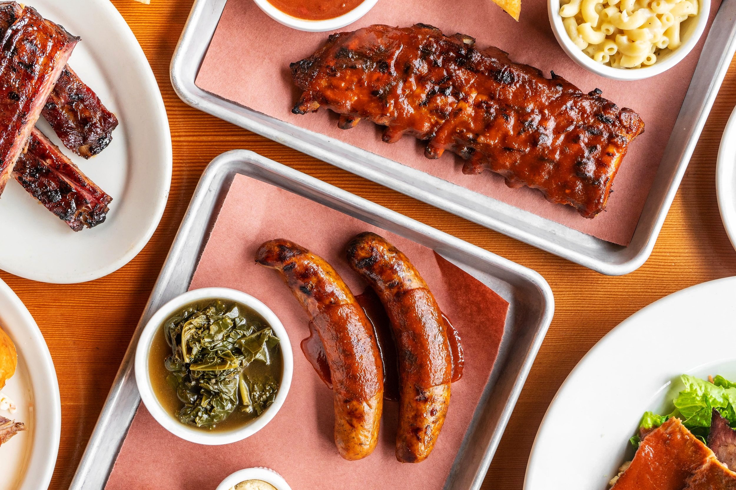 Barbecue ribs, sausage, and sides arranged on a wooden table